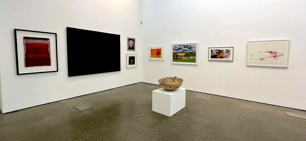 Installation shot from the 41st Members and Friends in 2025 exhibition | West Cork Arts Centre’s Members and Friends Exhibition 2026 | Saturday 20 June  – Thursday 16 July 2026 | Uillinn: West Cork Arts Centre | Installation shot from the 41st Members and Friends in 2025 exhibition (“The image above is taken from the 41st Members and Friends in 2025, when we celebrated 40 years of West Cork Arts Centre and 10 years at Uillinn.”) | fairly typical installation shot – we are looking towards a corner in a room with white walls and probably polished-cement floor; four artworks hang on the left wall, including one large, very dark one; the works on the right wall are smaller, and there is a pale-brown, cracked-pottern-style large bowl on a fairly low square, white plinth  