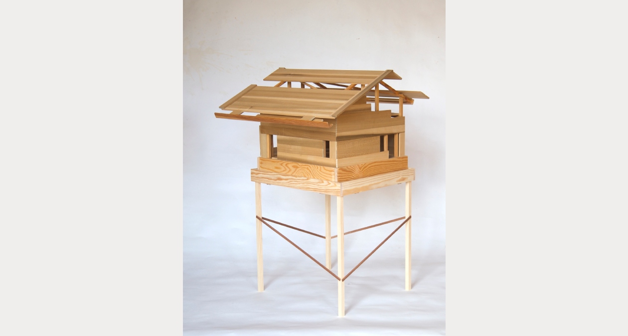 Adrian Duncan, Haus Alois, 2026, Tulipwood, deal, teak, 50 x 50 x 90cm, Image courtesy of the artist | Adrian Duncan: Buildings from a Novel | Friday 11 September 2026  – Sunday 10 January 2027 | Royal Hibernian Academy | Adrian Duncan, Haus Alois, 2026, Tulipwood, deal, teak, 50 x 50 x 90cm, Image courtesy of the artist | photo of a maquette of a buildig on stilts, all made of wood; floor plan appears to be square, bullding effectively one storey, though with slopig roofs with odd gaps and apparently some sort of construction, ziggurat-like, under it 